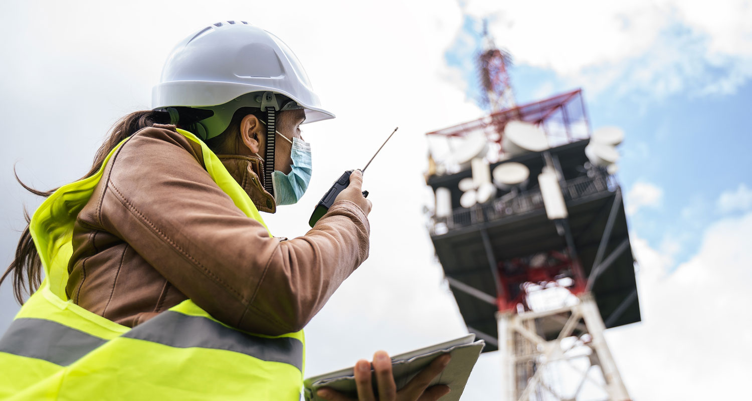 A construction worker wearing a facemask uses a radio to communicate with another worker.